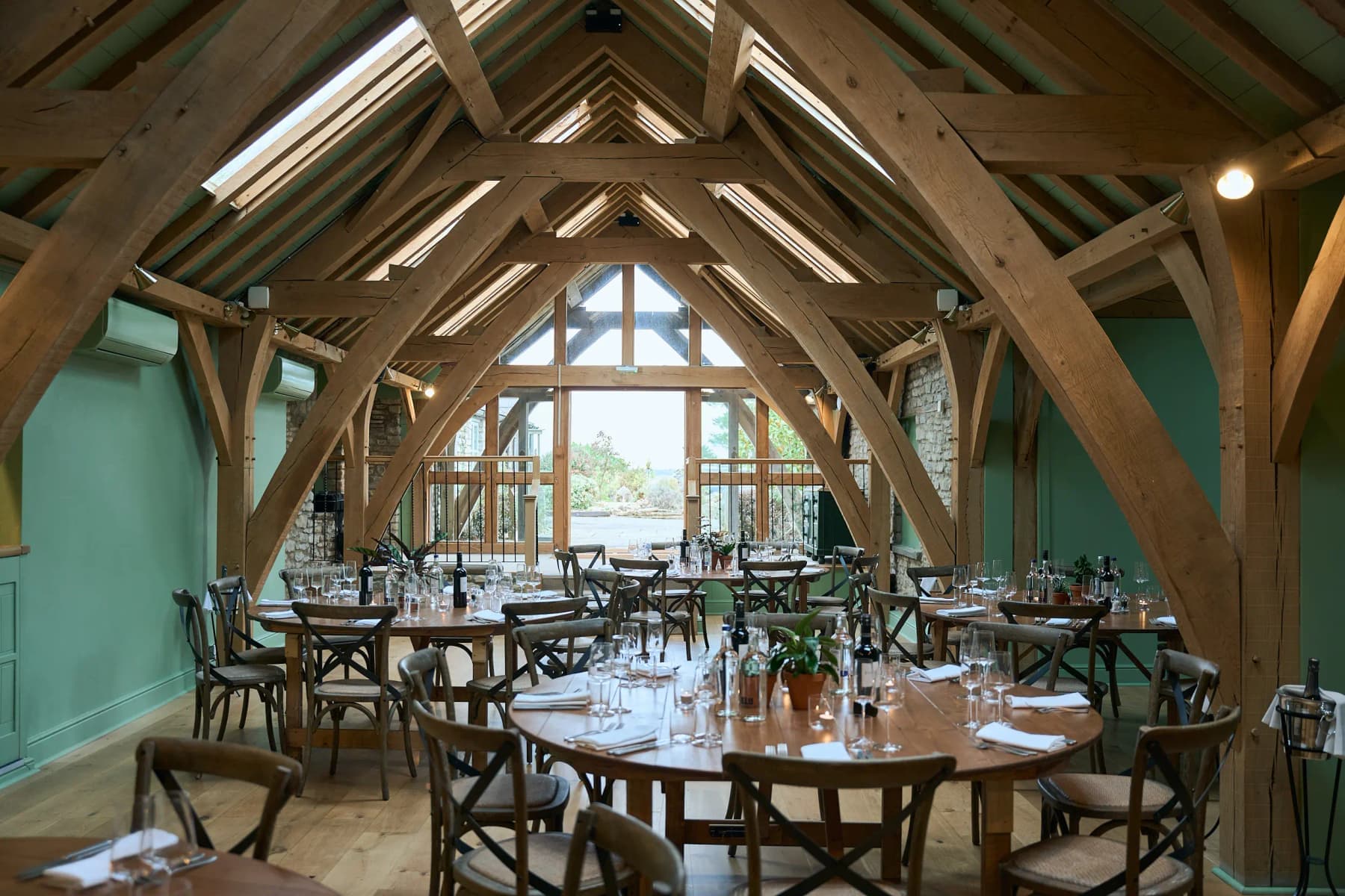 The oak-beamed workshop room at Mad Swans, set with round tables and a wall of glass looking onto the countryside